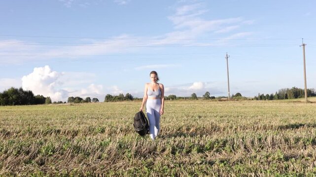 A woman with a backpack in sportswear walks through a field on a bright sunny day on a hike