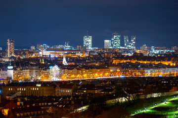 Obraz premium The Vltava Riverside with city lights shining in the evening. Pankrac stands tall in the background as the city comes alive at night.