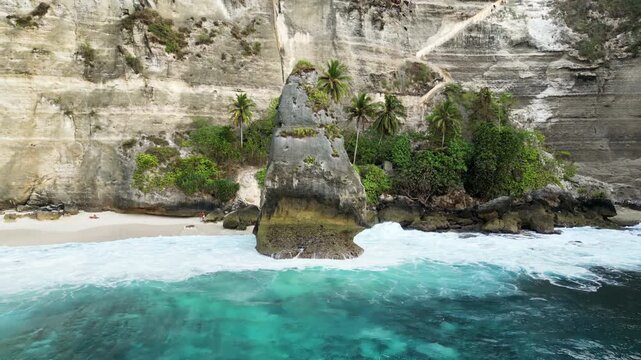 Aerial drone view of the iconic limestone rock formation at Diamond Beach, Nusa Penida, Bali, Indonesia. Turquoise waves crash against the massive sea stack surrounded by towering white cliffs and tro
