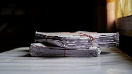 Stack of old newspapers tied with string on wooden table in dim light © AsikurRahman