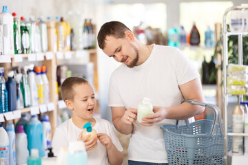 Family schoolboy son and dad are choosing liquid hand soap in store. Customer reads label, compare...