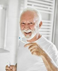 Portrait of an elderly senior man is cleaning brushing his teeth in front of mirror in bathroom....