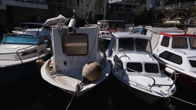 White small fairytale fishing boats rocking in the harbour of Lovran, Croatia. Real time side view of an Adriatic Sea port. Sunny spring day in the Kvarner Bay. Everyday life in a travel destination.