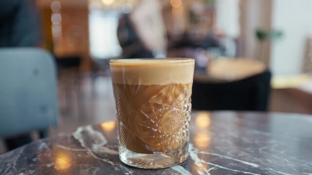 Latte on marble with golden crema. Sophisticated cafe scene showcasing glass of latte with intricate embossing and warm lighting