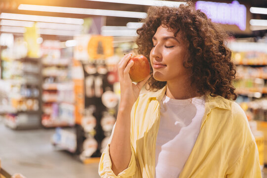 Woman enjoying the fresh scent of a ripe apple in the supermarket, embracing mindful shopping and healthy eating