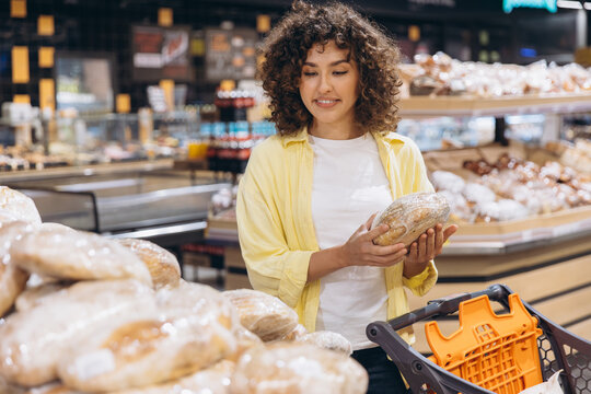 Young woman shopping for fresh bread in a modern supermarket, choosing items from the bakery section on daily errands