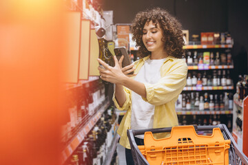 Young woman scanning wine bottle with smartphone app in supermarket, shopping groceries for home