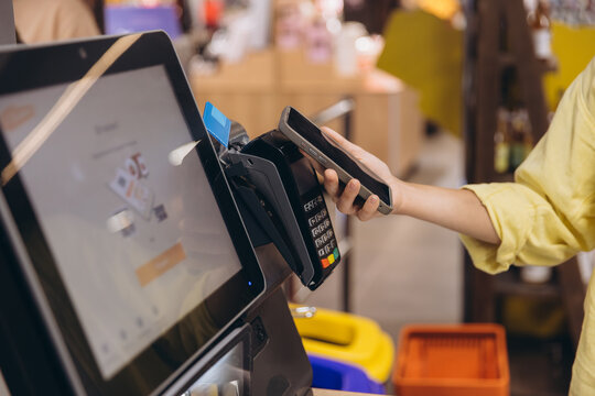 Person making a secure contactless payment using a smartphone at a point of sale terminal in a store, digital transaction