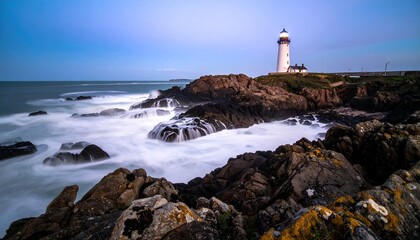 Obraz premium Dramatic long exposure of a lighthouse on a rocky coast with crashing waves at dusk.
