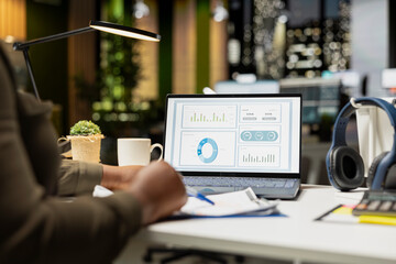 African american skilled analyst reviewing monthly reports for a new growth strategy, using infographics on laptop to plan resources allocation and align objectives with financial development.