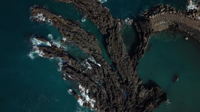 Cinematic aerial orbit over Seixal natural lava pools, ocean waves crashing against black volcanic rocks with white foam, Madeira coastline, 4K.