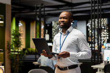 Fototapeta premium Portrait of cheerful businessman in office managing schedules on laptop, organizing calendar appointments and meetings. Jolly African american man compiling company information records on notebook