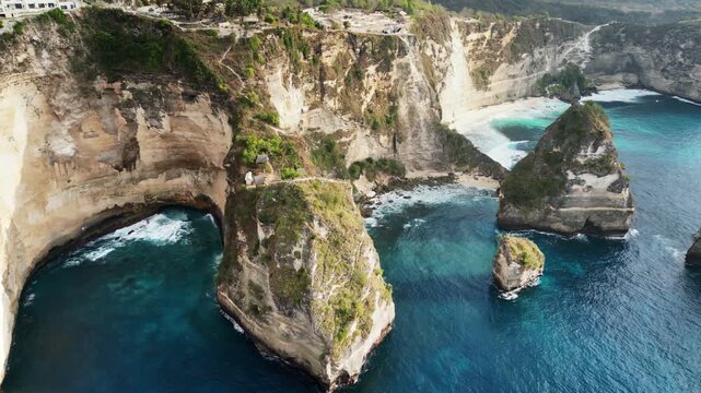 Aerial drone view of Kelingking Beach in Nusa Penida, Bali, Indonesia. Dramatic limestone cliffs tower above a pristine white sand beach and vibrant turquoise water. The famous T-Rex shaped headland d