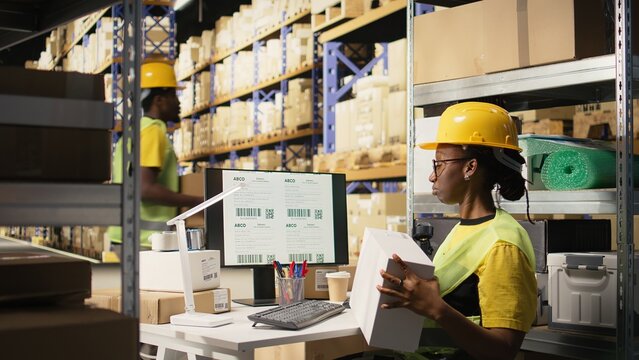 African american female verifying the shipment details on awb labels, using package tracking software system with accurate order status. Monitoring import export operations in depot. Camera A.