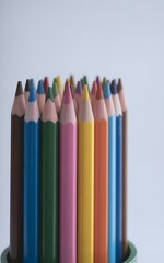 Naklejka premium Vibrant collection of sharpened colored pencils stands upright in a green container against a light backdrop