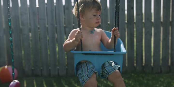 Young child sitting in a swing holding a rope toy