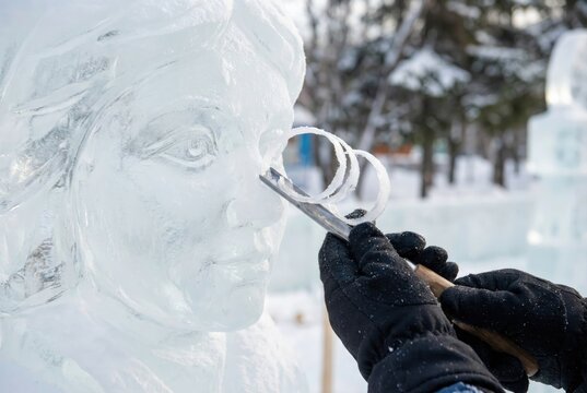 Ice sculptor using a chisel to carve fine details on a female face statue out of ice