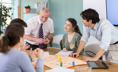 Positive young students and a teacher playing educational board game during a classroom workshop