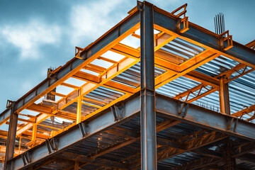 Fototapeta premium Steel frame structure of a modern building under construction against a dramatic sky. Industrial architectural background featuring iron beams, metal pillars, and girders at sunset