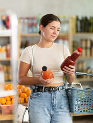 While shopping in grocery store, young woman buyer choosing juice. Clients look package of fruit...