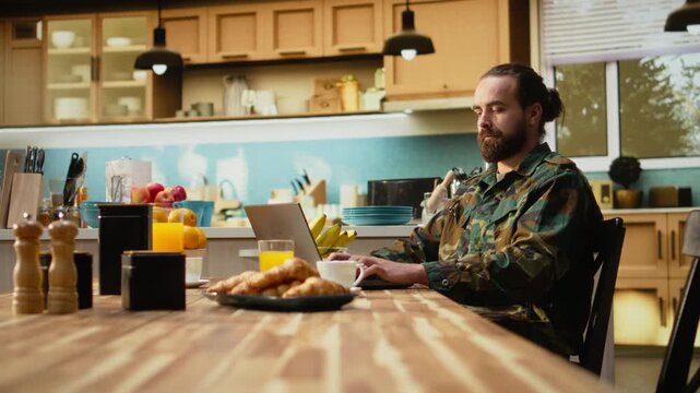 Off duty serviceman in military uniform with laptop and coffee at home, calm morning routine with breakfast pastry and orange juice. Domestic life and relaxation, quiet moment indoors.