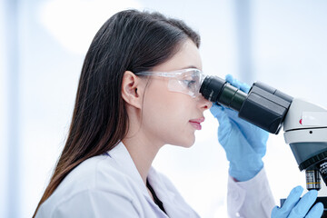 Fototapeta premium Medical pathologist looking through microscope eyepiece for cancer diagnosis. Female scientist in safety glasses analyzing biopsy slide in sterile hospital lab carefully.