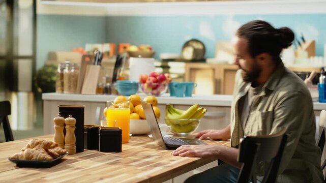 Remote work concept, morning coffee, adult man using laptop, rustic kitchen with natural light helps solve daily tasks. Digital nomad lifestyle does online productivity, modern interior.