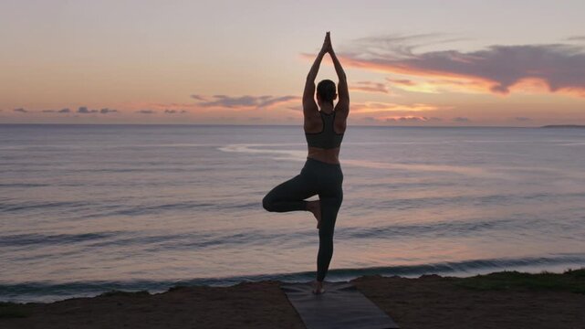 Woman practicing yoga tree pose on a cliff during sunset
