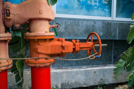 Close up of red fire department gate valves and piping system installed outdoors near a building with glass windows.