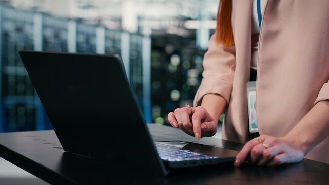 Close up of engineer typing on laptop in server farm, doing network management virtualization. Data center admin overseeing large scale IT infrastructure supercomputers with notebook, camera B