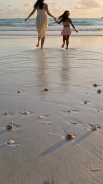 Mother and daughter holding hands walking on a sandy beach at sunset