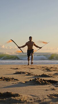 Muscular fire dancer performing with flaming swords at sunset on the beach