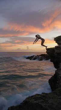 Adventurous couple cliff jumping into the ocean at sunset