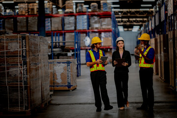 Fototapeta premium Smiling diverse warehouse team having a positive discussion. Female manager and industrial workers collaborating happily on logistics management.