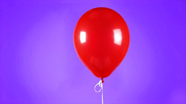 A shiny red latex balloon with a white string isolated against a solid purple background. Ideal for festive designs, birthday greetings, and colorful motion graphics.
