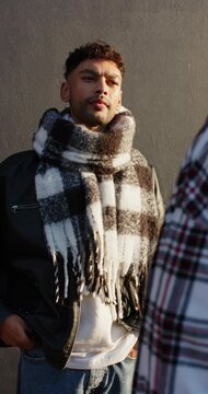 Vertical video: Man in jacket hearing friend's remark, adjusting checkered scarf for warmth outside