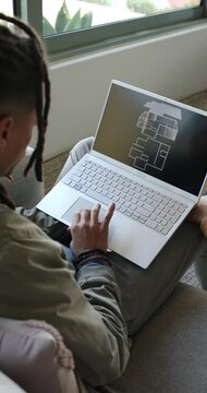 Vertical video: Man is opening laptop on couch near window, and is panning floor plan for review