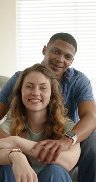 Vertical video: Diverse couple embracing on couch sharing intimate glance sparking warm smile