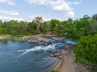 Top-down drone photograph of Kaeng Tana Pat rapids in Sakon Nakhon, Thailand. Clear flowing water over rocky formations with a small sandy beach. © 2D_Jungle