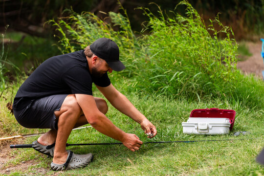 Fisherman at edge of an inland brook getting fishing rod line ready to fish with