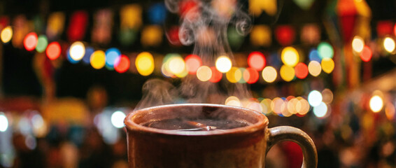 Fototapeta premium A cup of hot chocolate with steam rising from it, set against a blurry background of colorful lights