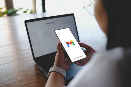 Bangkok, Thailand. March 17, 2026; A person holding a smartphone displaying the official Gmail logo, a popular email service by Google Workspace, while working at a wooden table.