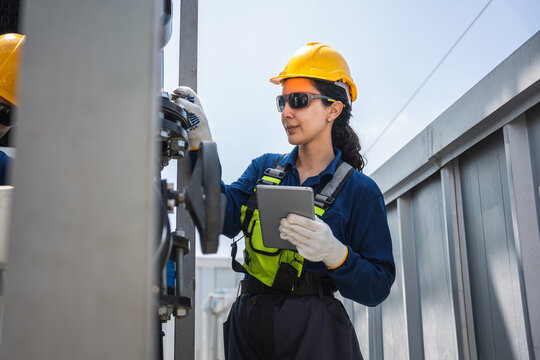 Female engineer in hardhat using digital tablet for industrial equipment inspection at factory, Professional worker performing maintenance check with tablet on industrial valve and pipeline system