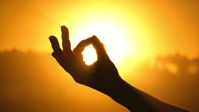 Silhouette of a hand performing the mudra gesture against a brilliant, radiant orange and yellow sunset sky symbolizing peace enlightenment and spiritual connection