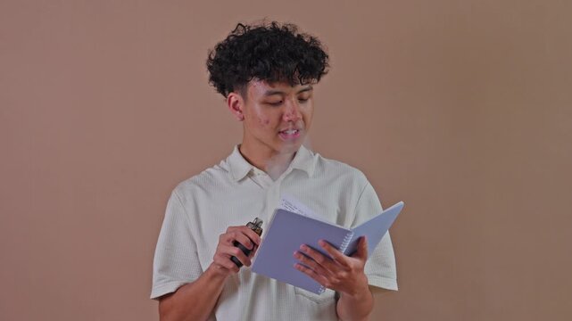 Young Asian man smoking e-cigarette while reading notebook in studio