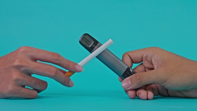 Hands crossing cigarette and electronic vape device over solid turquoise background
