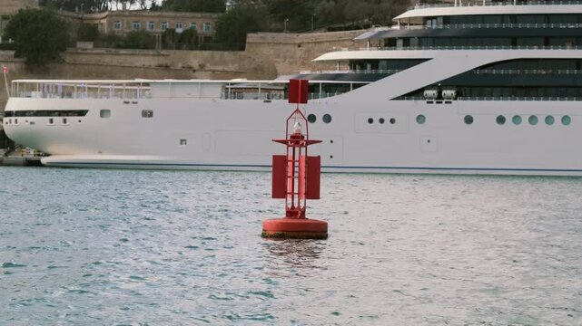 Huge steel industrial buoy swaying on waves with a ship and city skyline background
