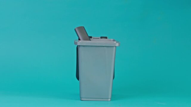 Hand drops various electronic cigarettes into small trash isolated on turquoise background