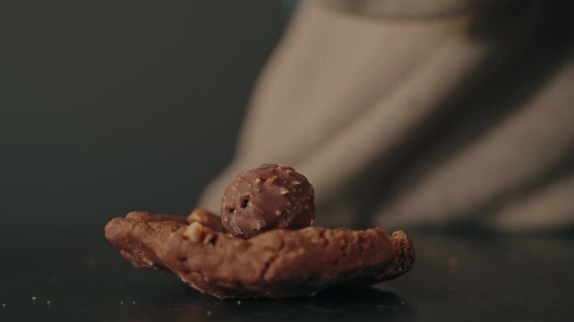 Closeup of hand placing chocolate ball topping onto cookie biscuit on table surface during dessert preparation