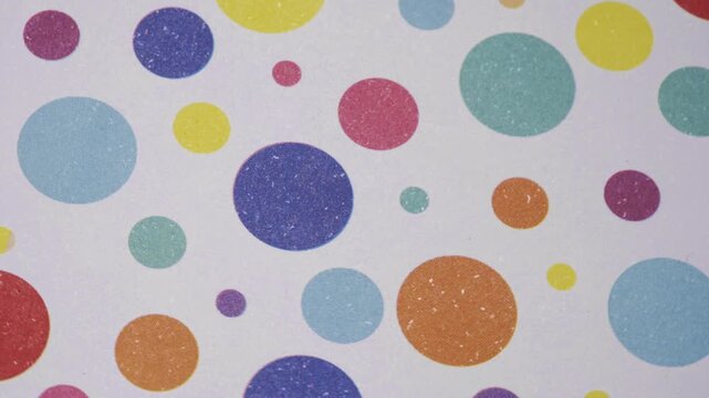 Top view of colorful polka dot pattern in motion on white textured paper, Rotating multicolored circle pattern background on white grainy paper texture